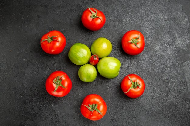 Top view red and green tomatoes around a cherry tomato on dark ground with copy space