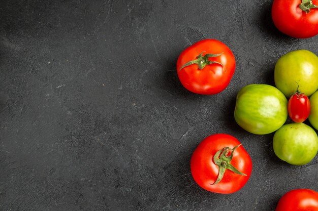 Top view red and green tomatoes around a cherry tomato on the right of dark ground with copy space