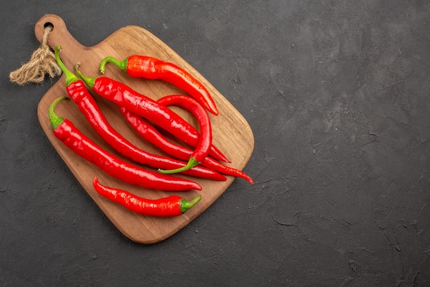 Top view red hot peppers on a diagonal chopping board at the left side of the black table with copy space