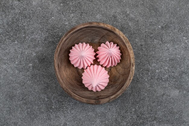 Top view of red meringues in wooden bowl over grey surface