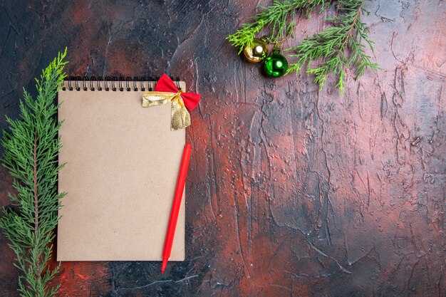 Top view red pen on a notebook pine tree branches xmas tree ball on dark red surface free space