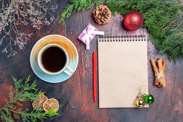 Top view red pen a notebook pine tree branches xmas tree ball toys cinnamon sticks a cup of tea on dark red surface xmas photo