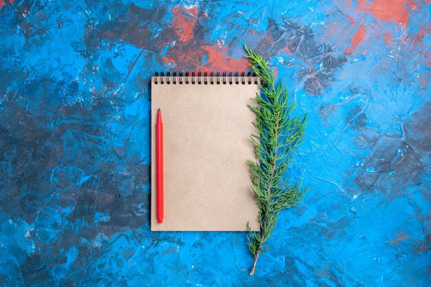 Top view red pencil on a notebook pine tree branch on blue surface free place