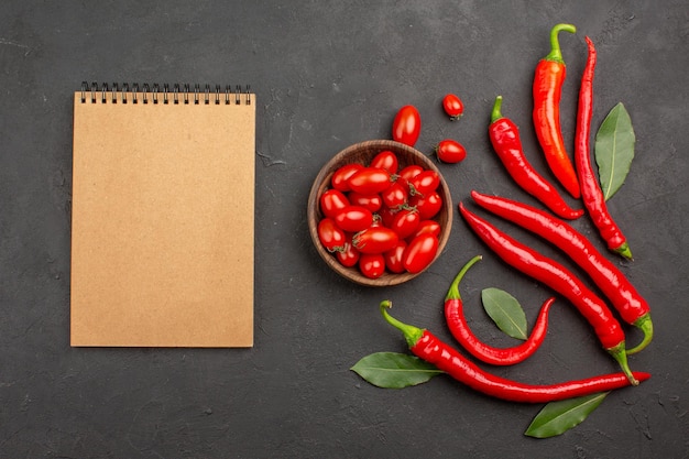 Free Photo top view red peppers and pay leaves and a bowl of cherry tomatoes and a notebook on black table