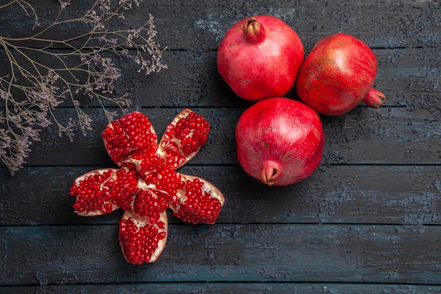 Top view red pomegranates pilled pomegranate next to tree branches and three pomegranates on dark surface