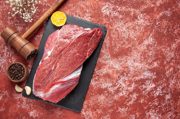 Top view of red raw fresh meat lemon on black board and brown wooden hammer pepper on pastel red background