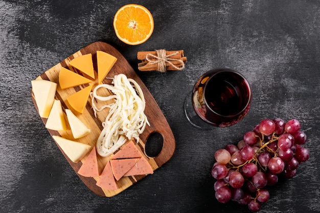 Free Photo top view of red wine with grape, orange and cheese on wooden cutting board on dark surface horizontal