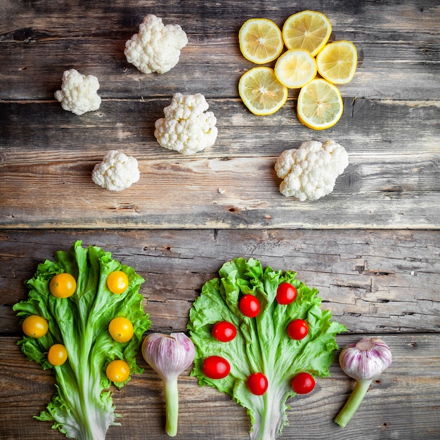 Top view red and yellow tomatoes with lettuce, cauliflower, lemons, garlic on dark wooden background.