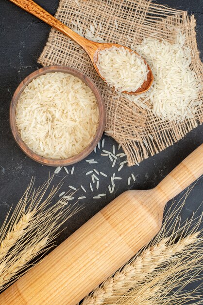 Top view rice in bowl and wooden spoon rolling pin on black table