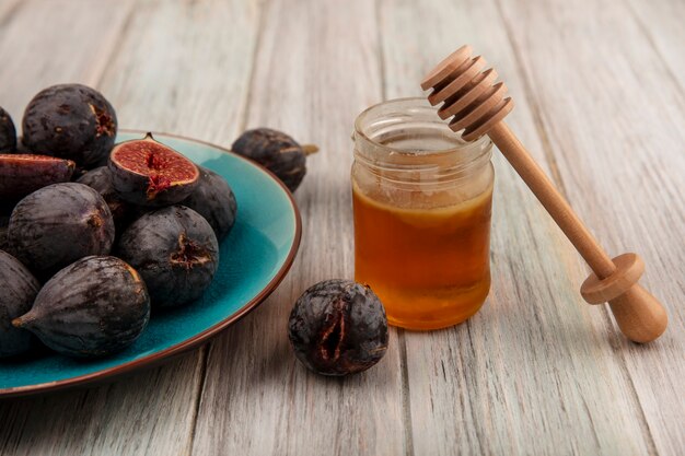 Top view of ripe black mission figs on a blue dish with honey in a glass jar and honey spoon on a grey wooden surface