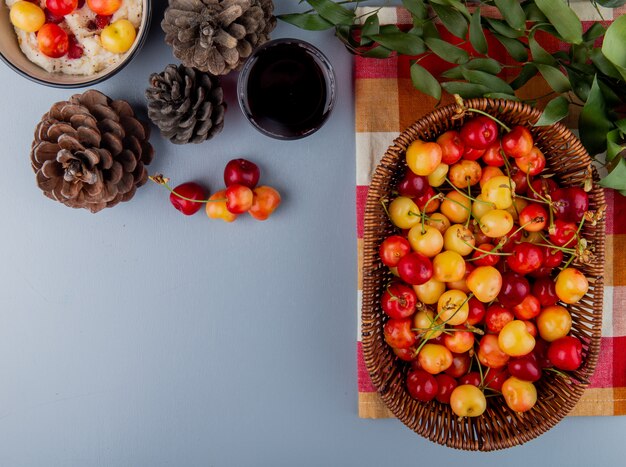 Top view of ripe rainier cherries in a wicker basket a glass of juice and cones on grey with copy space