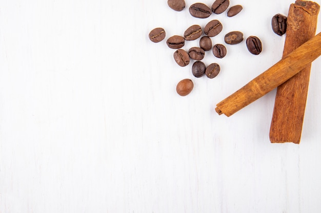 Top view of roasted coffee beans and cinnamon sticks on white wooden background with copy space