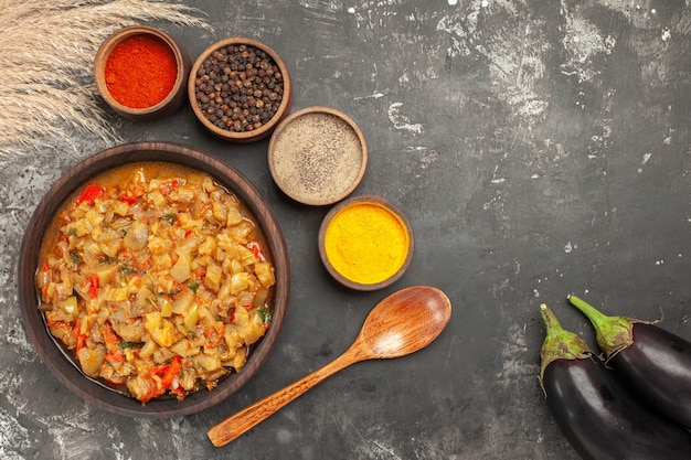 Free photo top view of roasted eggplant salad in bowl and different spices in small bowls wooden spoon eggplants on dark surface