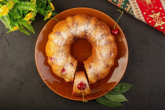 A top view round cherry cake inside brown plate on the dark table cake biscuit sugar sweet