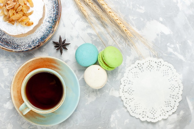 Top view round little cake sugar powdered with raisins tea and macarons on the white surface