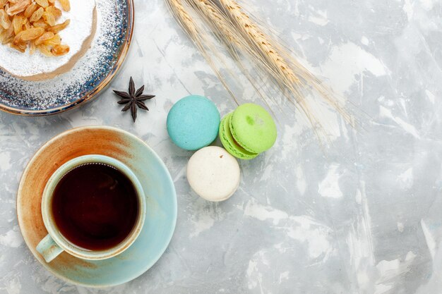 Top view round little cake sugar powdered with raisins tea and macarons on white surface