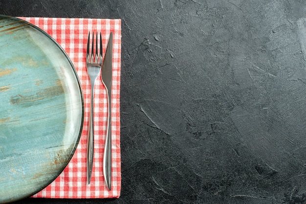 Free Photo top view round platter dinner knife and fork on red and white checkered napkin on black table with free space