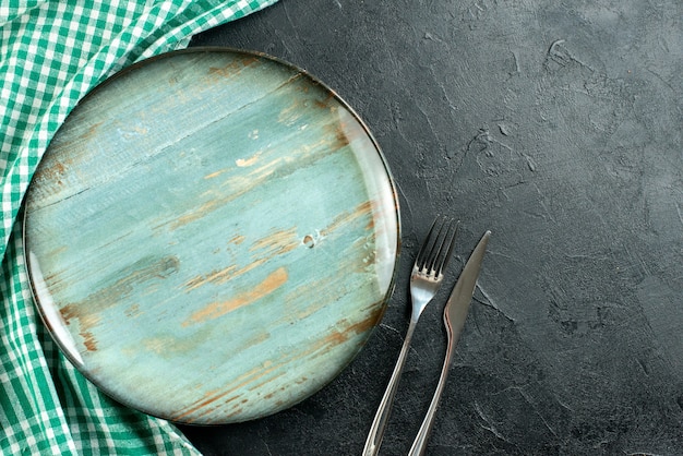 Free photo top view round platter fork and knife green and white tablecloth on black table free space