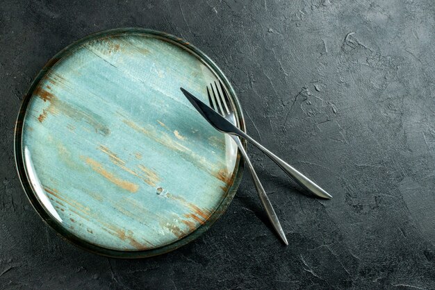 Top view round platter steel fork and dinner knife on black table with free place