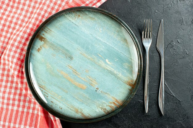 Top view round platter steel fork and dinner knife red and white checkered tablecloth on black table