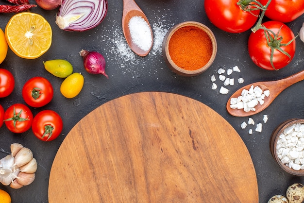 Top view round wood board salt in wooden spoons garlic cumcuats tomatoes lemon on dark table