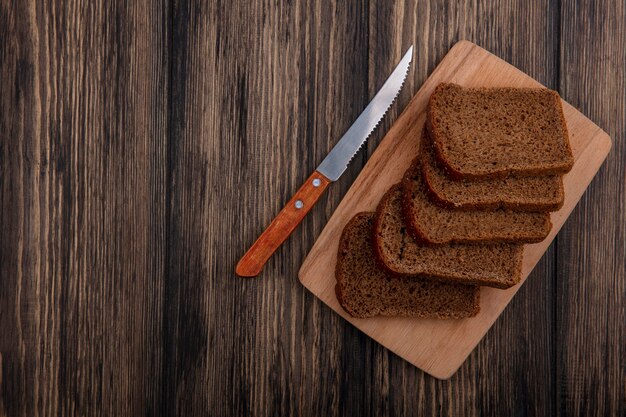 Top view of rye bread slices on cutting board and knife on wooden background with copy space