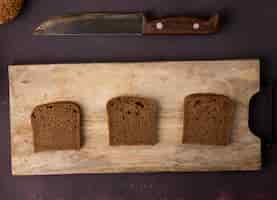 Free photo top view of rye bread slices on cutting board with knife on maroon background