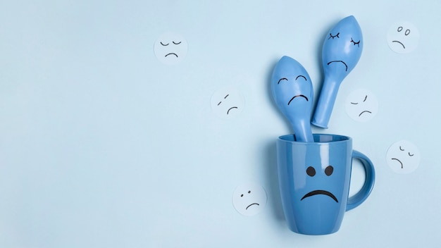 Free photo top view of sad mug with balloons with frowns for blue monday and copy space