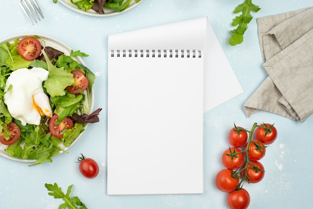 Top view salad with fried egg and tomatoes with blank notepad