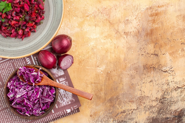 Top view salad with green leaves and vegetables made of bowl of chopped cabbage and onions on a wooden table with copy place on the left