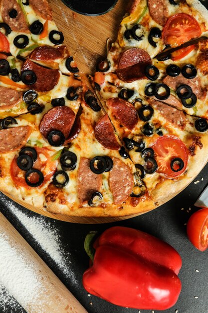 Top view salami pizza on stand with tomatoes olives and bell peppers on black table