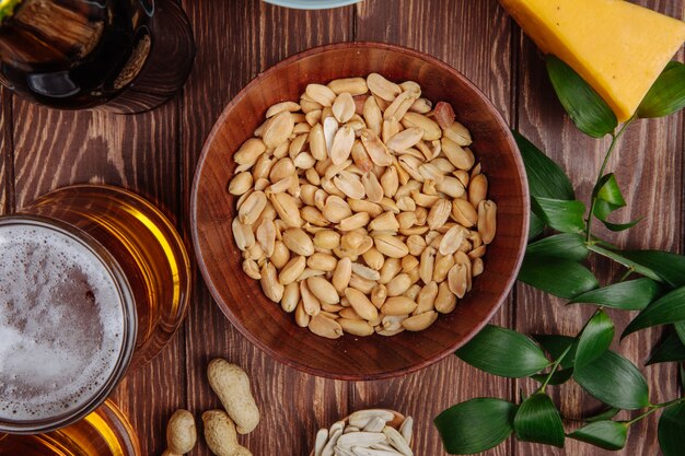 Top view of salty snacks peanuts in a wood bowl with a mug of beer on rustic wood