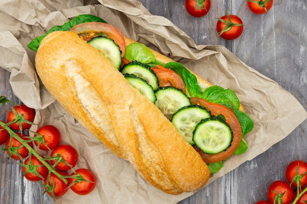 Free photo top view of sandwich on paper with tomatoes and cucumber slices