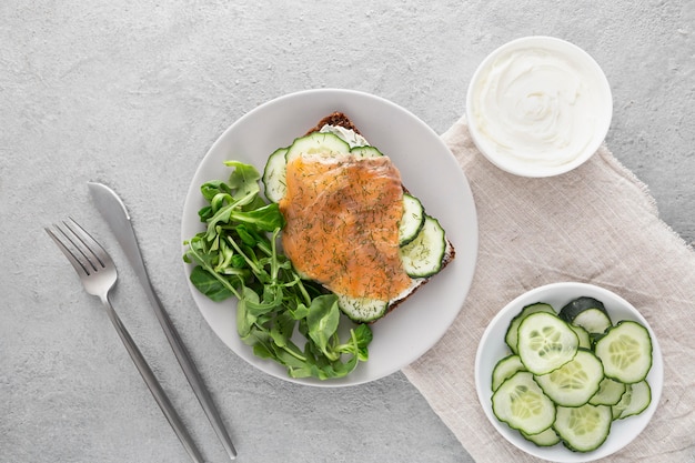 Top view sandwich with cucumbers and salmon on plate with cutlery