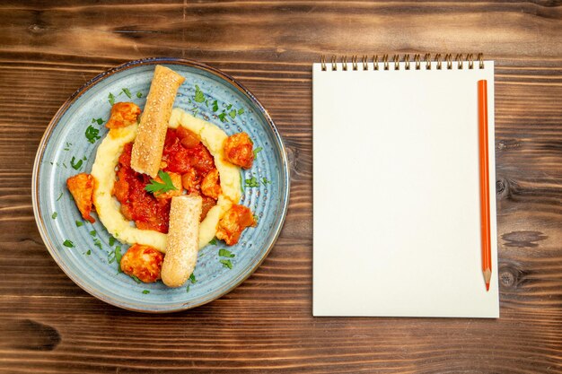 Top view of sauced meat with mushed potatoes and sliced bun on brown wooden table