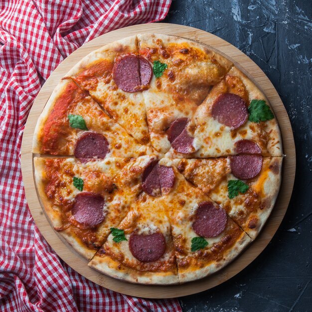 Top view sausage pizza with napkin in board cookware