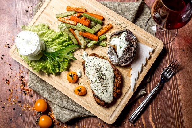 Top view schnitzel with cream cheese with baked potatoes in foil and with vegetables on a board