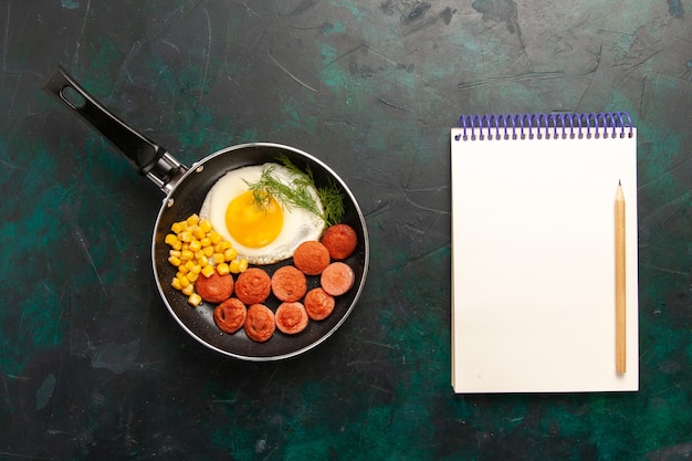 Free photo top view scrambled eggs with sliced sausages and notepad on the dark background