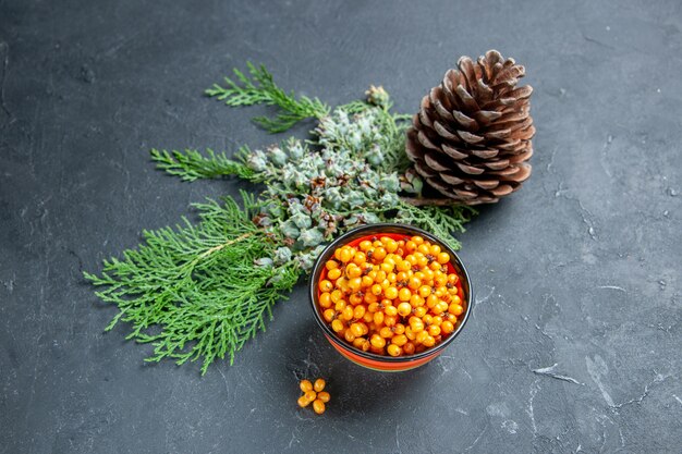 Top view sea buckthorn in bowl pine branch pinecone on dark red table free place