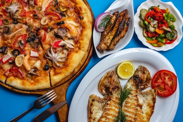 Top view seafood mix pizza with octopus mushrooms crab meat tomato cheese fried fish with slice of lemon red onion and vegetable salad on the table