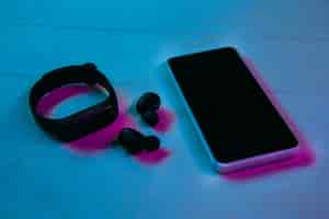 Free photo top view of set of gadgets in purple neon light and blue background. smartphone, smartwatch and wireless headphones on wooden table. copyspace for your advertising. tech, modern, gadgets.