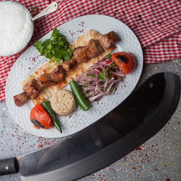 Free photo top view shish kebab with fried vegetables and chopped onion and ayran and knife in white plate