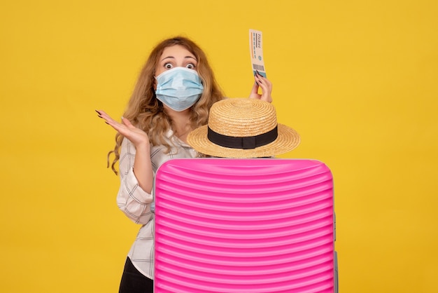 Free photo top view of shocked young lady wearing mask showing ticket and standing behind her pink bag