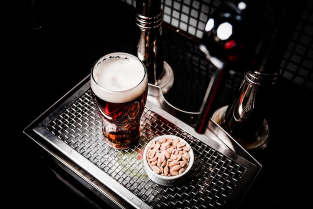 Free photo top view shot of a glass of lager beer with a cup of peanuts on a metal screen tray