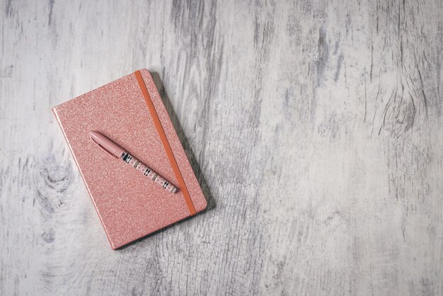 Top view shot of a glitter-covered notebook with pen on the gray wooden background with copy space