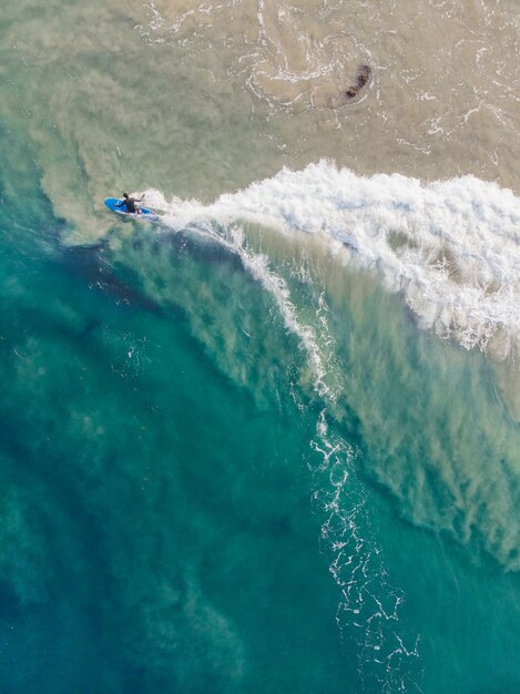 Top view shot of a person with a surfboard swimming in Varkala Beach