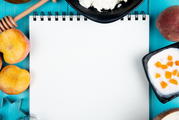 Top view of a sketchbook and fresh ripe peaches cottage cheese yogurt and cookie cutters arranged on blue