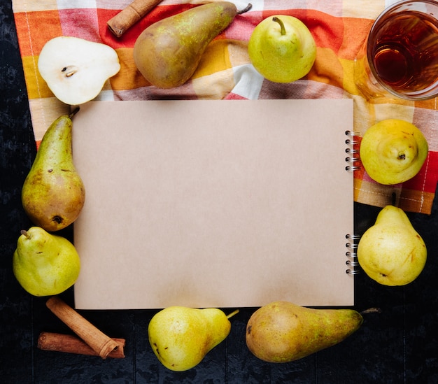 Free Photo top view of a sketchbook and fresh ripe pears arranged around with a glass of pear juice on black background