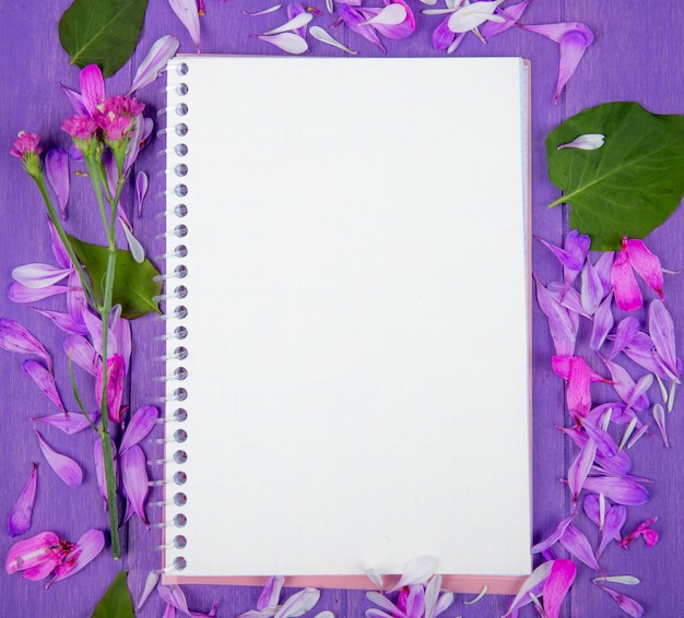 Free photo top view of a sketchbook and purple flower petals scattered around on purple wooden background