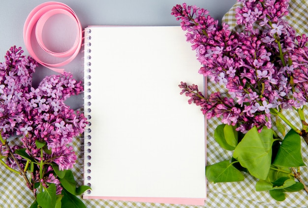 Free photo top view of a sketchbook with lilac flowers on plaid fabric on white background